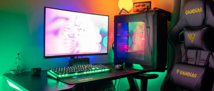 A colorful gaming setup featuring a PC, monitor, and gaming chair with RGB lights in a dark room.